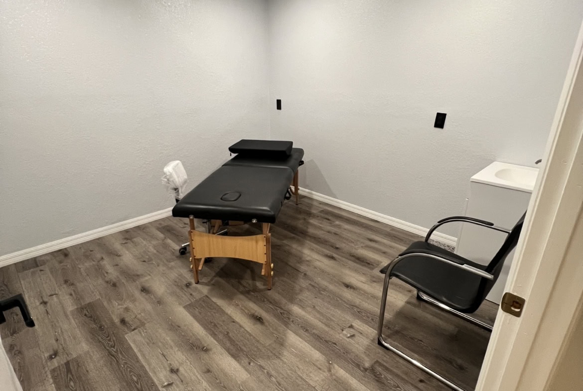 Small massage therapy room with treatment table and chair, ideal for salon or spa rentals.