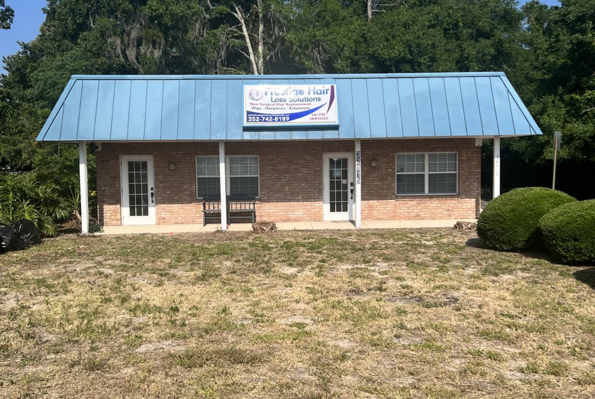 Modern salon building with blue metal roof and brick exterior, located in a natural setting.