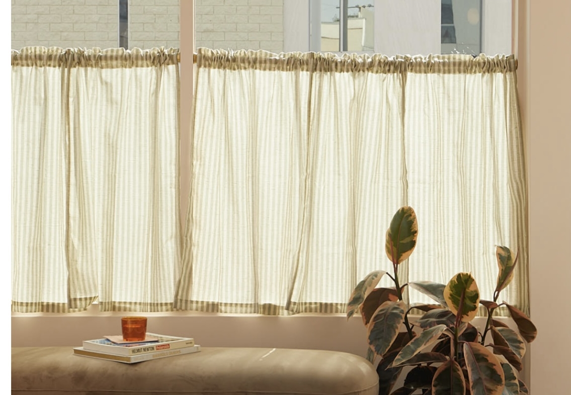 Alt text: Cozy salon waiting area with beige plush bench, potted plant, and window curtains.