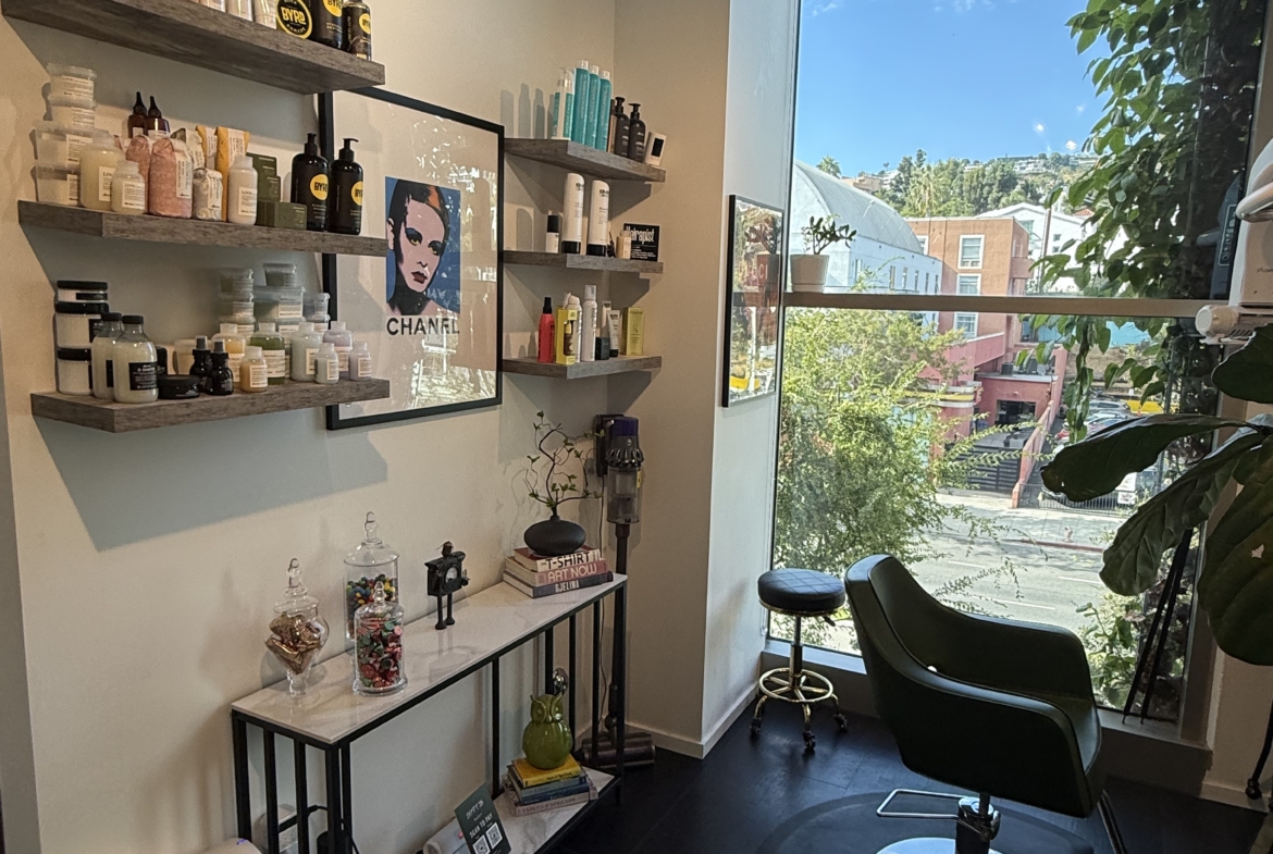 Bright salon with professional hair care products, stylish decor, and a large window overlooking the city.