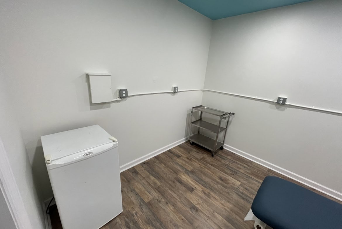 Clean salon rental room with white walls and wood flooring, simple furniture, ideal for beauty professionals.