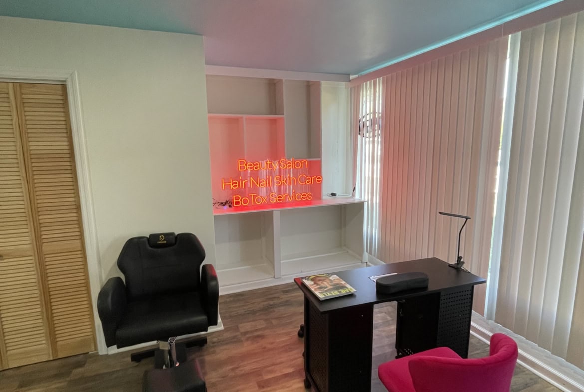 Modern salon reception area with furniture, neon sign, and natural light.
