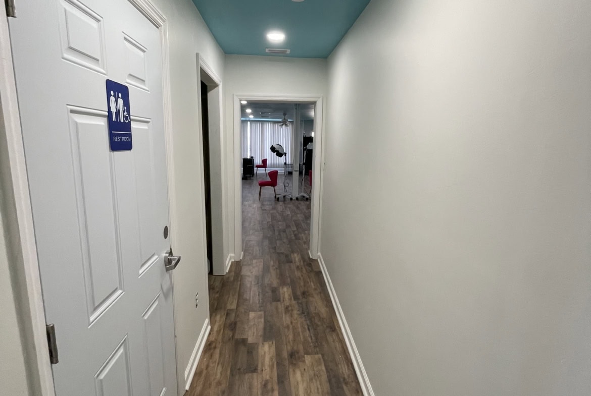 Bright hallway leading to salon treatment area with modern decor and wood flooring.