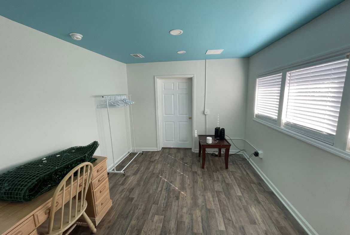 Bright, empty salon space with large windows, wooden flooring, and a vibrant blue ceiling.