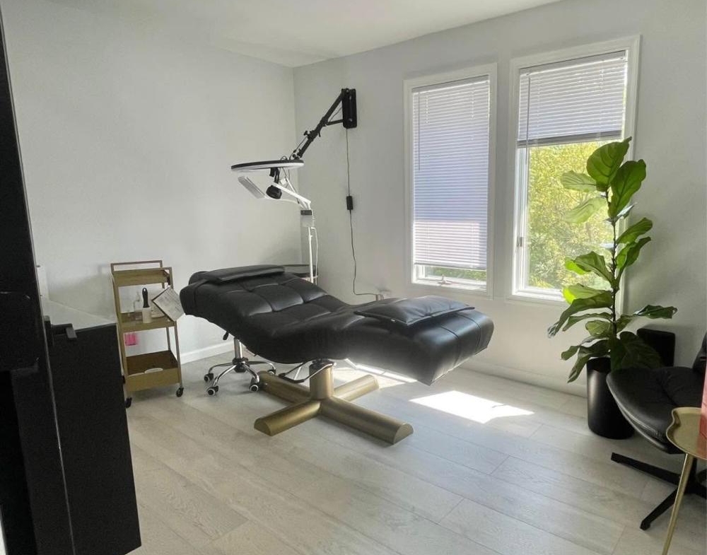 Bright salon space featuring a massage bed, large windows, and stylish decor.