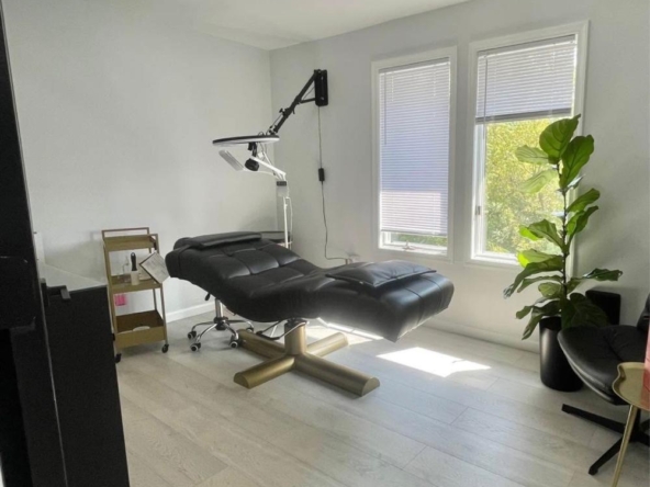 Bright salon space featuring a massage bed, large windows, and stylish decor.