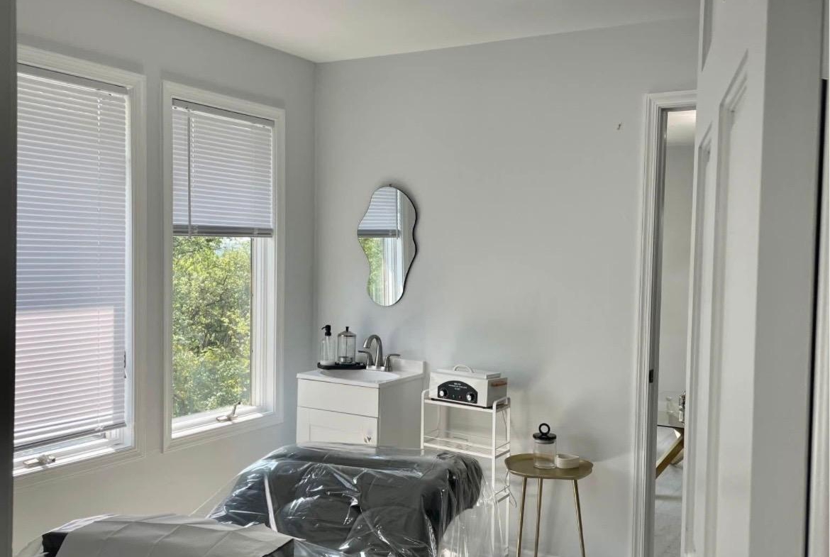 Bright salon treatment room with massage bed, minimalist decor, and natural light.