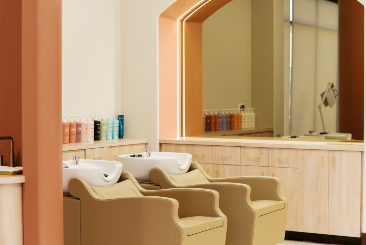 Bright salon wash area featuring beige chairs and large mirror for client comfort.