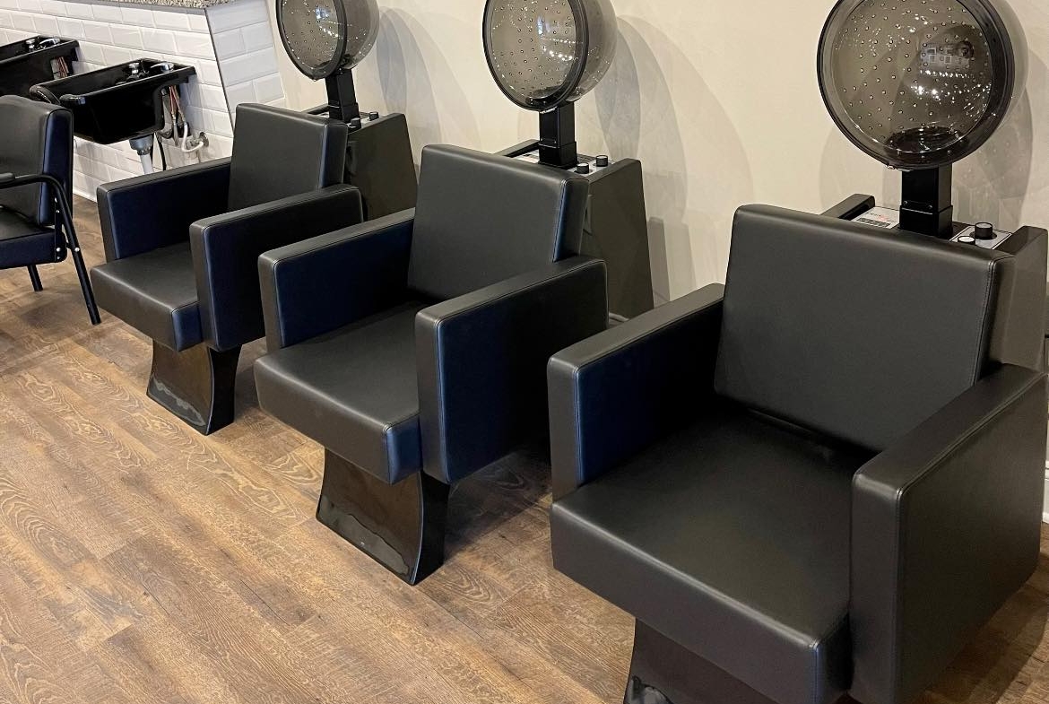Comfortable black salon chairs with built-in hair dryers for clients' hair washing needs.
