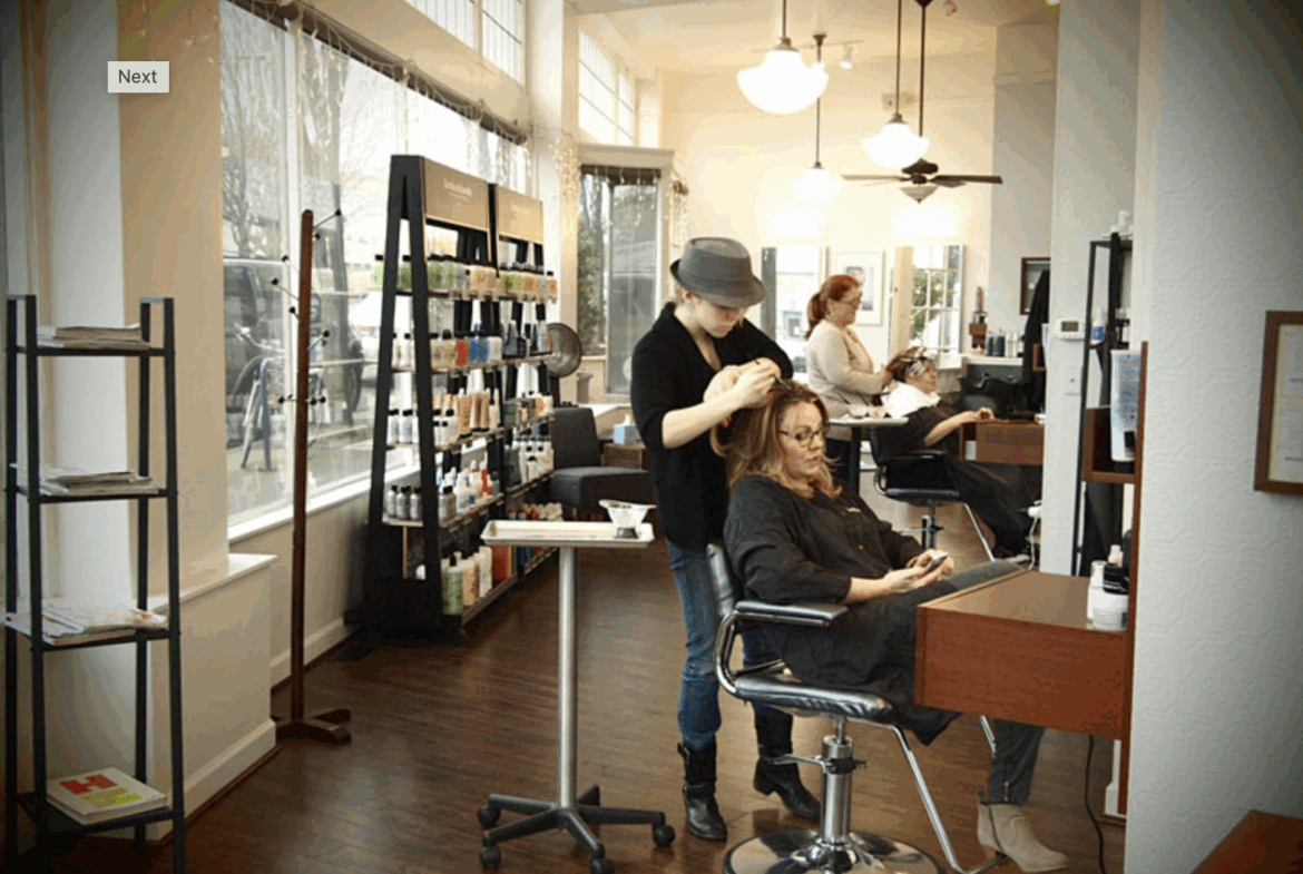 Bright, modern hair salon with stylist styling hair, comfortable client chair, hair products, and natural lighting.