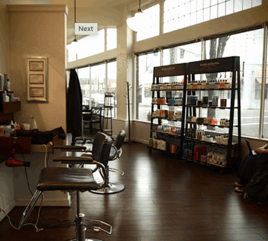 Bright salon interior studio with styling chairs, shelves with hair products, large windows, and natural light.