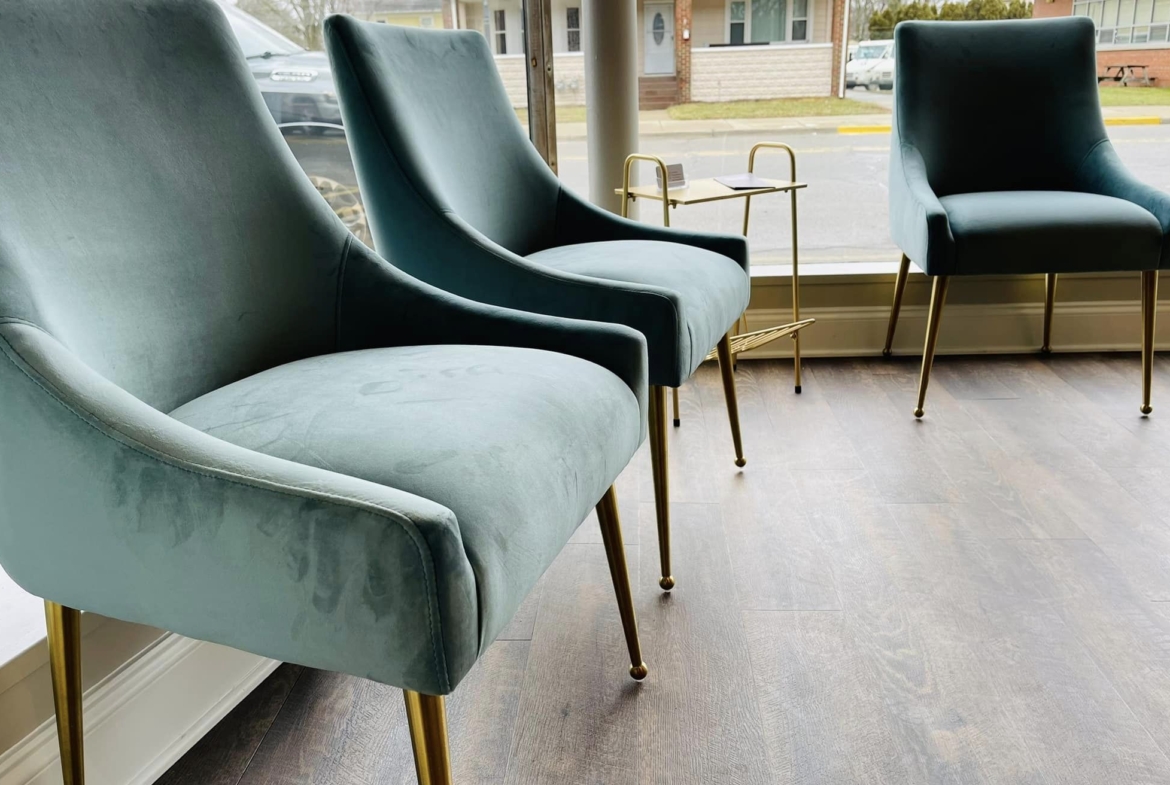 Luxurious teal velvet lounge chairs with gold legs in a modern salon waiting room.