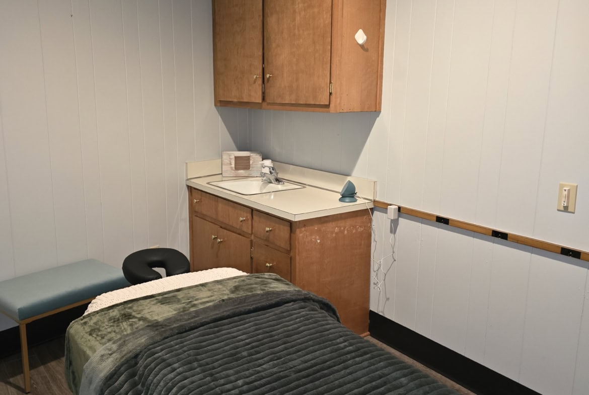 A massage therapy room with a massage table, wooden cabinets, and minimal decor in a salon or spa setting.