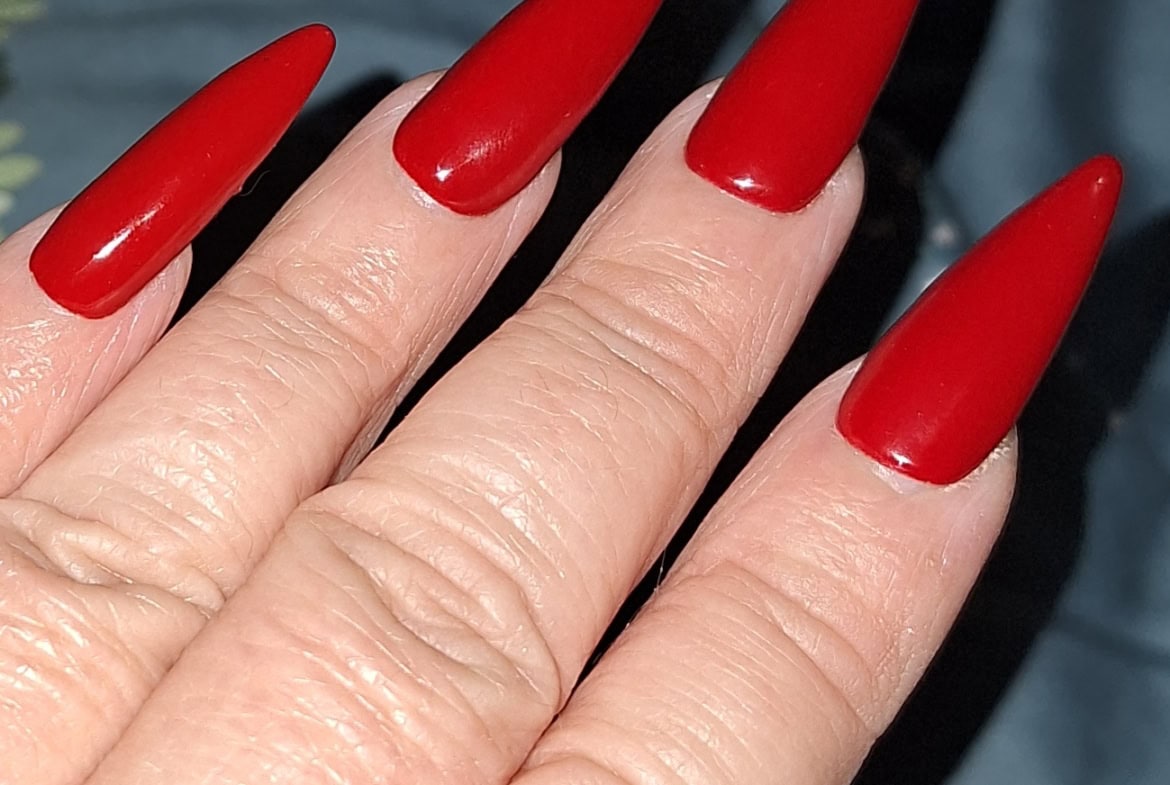 Close-up of long, sharp, red acrylic stiletto nails on a manicured hand.