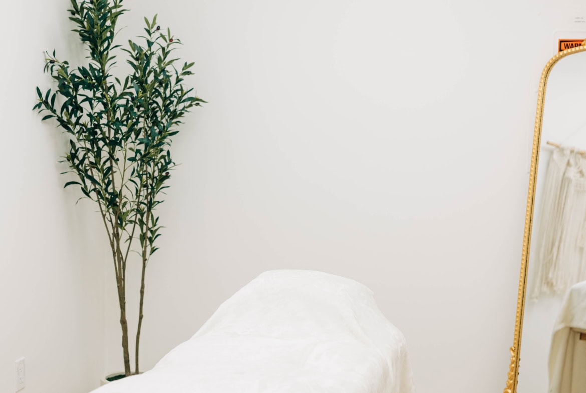 Relaxing massage table with white linens, modern decor, and a decorative mirror in a salon setting.