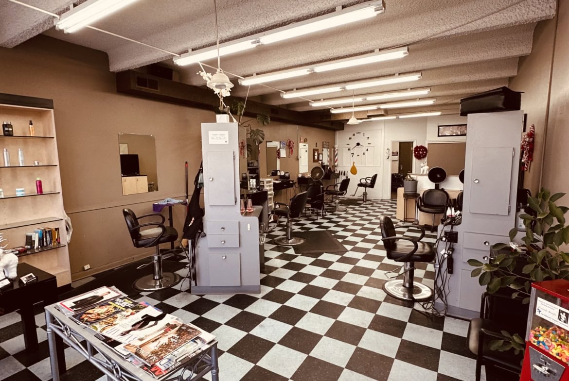 Spacious, well-lit salon with black and white checkered floors, styling chairs, and hair stations.