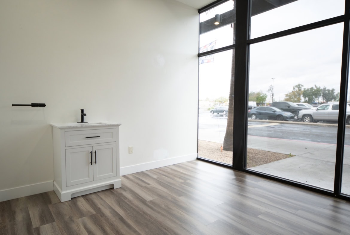 Bright empty salon space with large windows, wooden floors, and minimal decor.