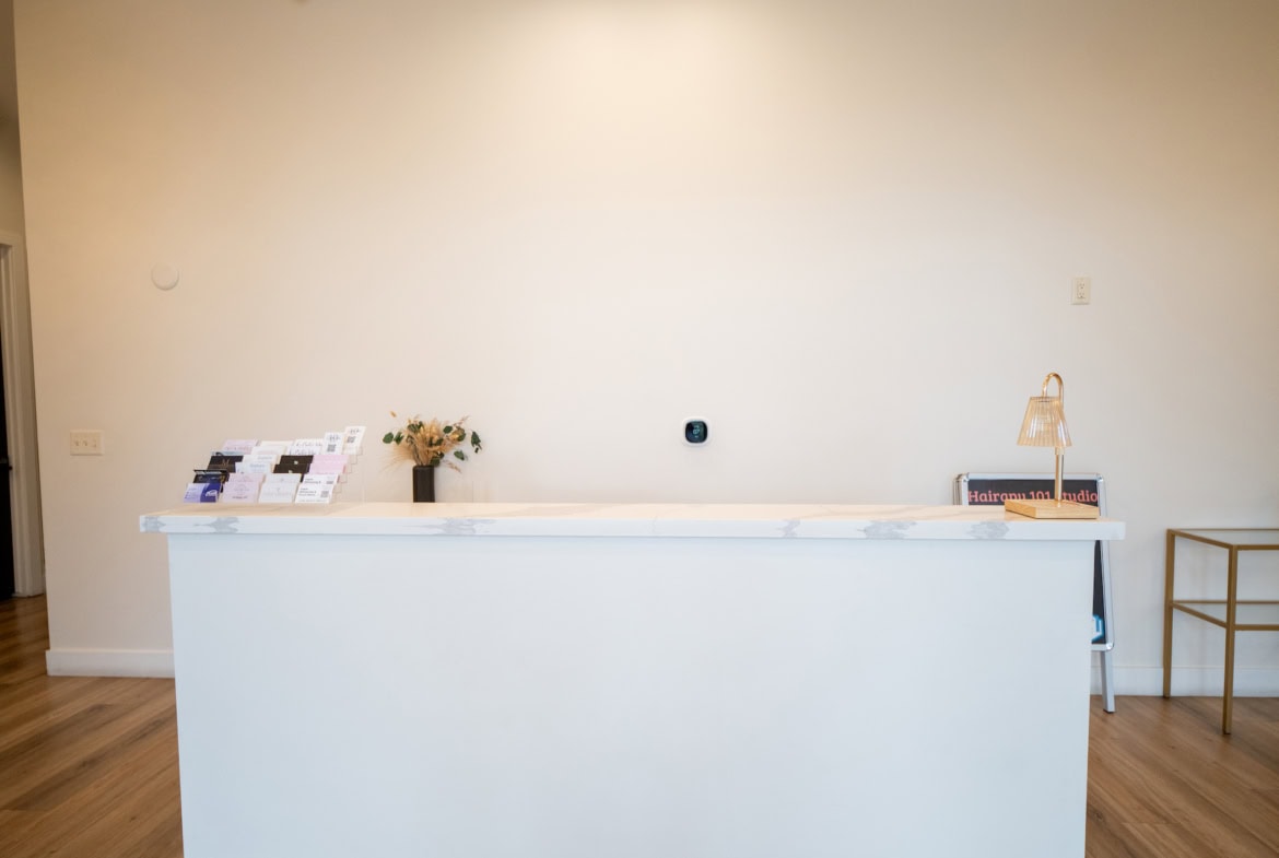 Bright salon reception with minimalist design, white countertop and warm wood flooring.