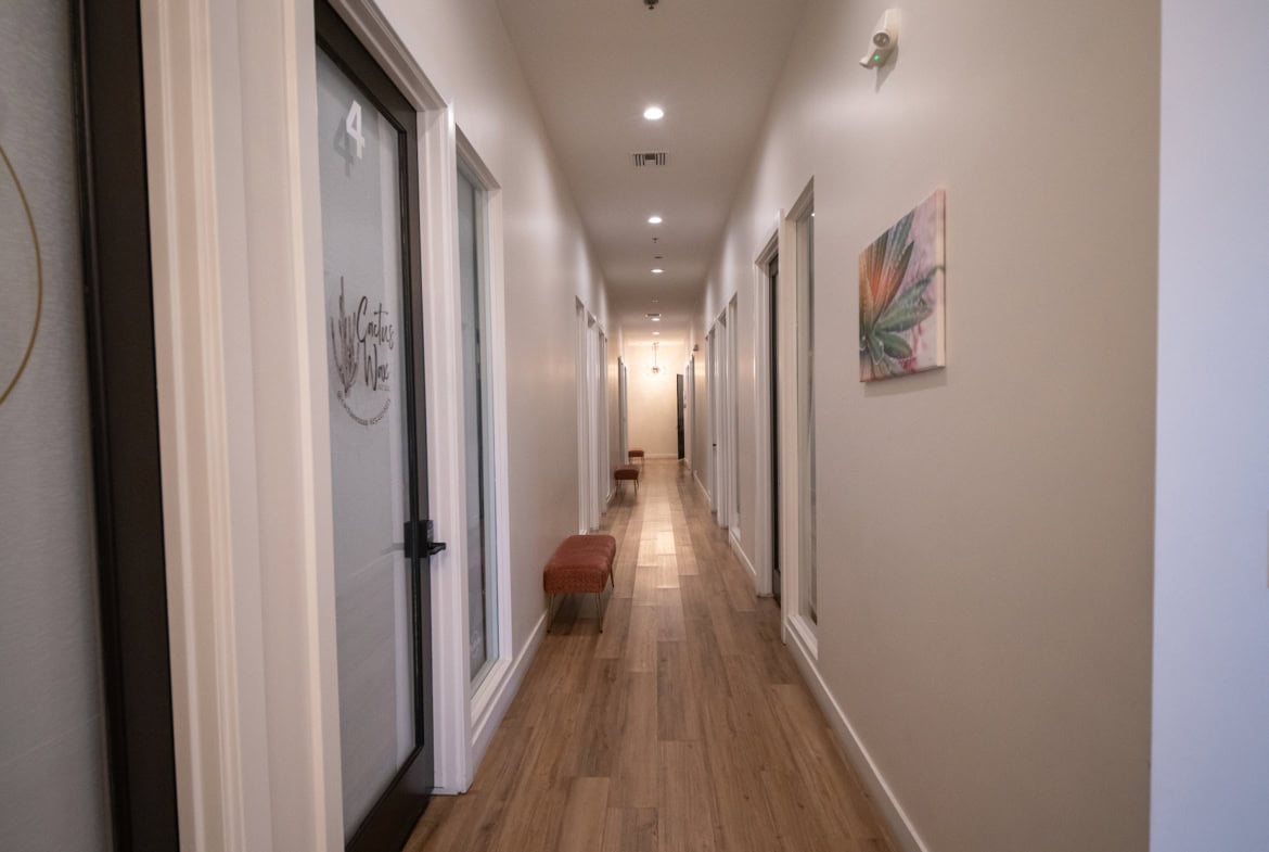 Bright, inviting salon corridor with private rooms, stylish art, and wooden flooring.
