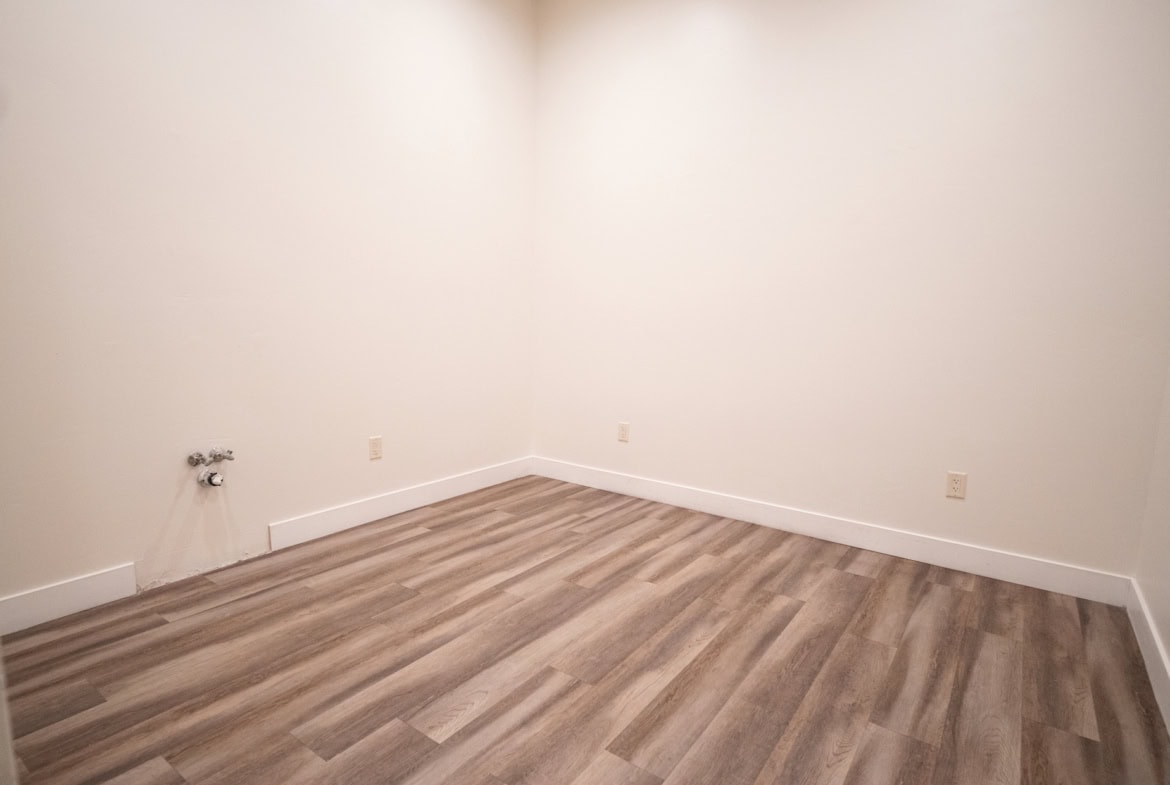 Bright, clean empty room with wood floors and neutral white walls for salon or studio rental.