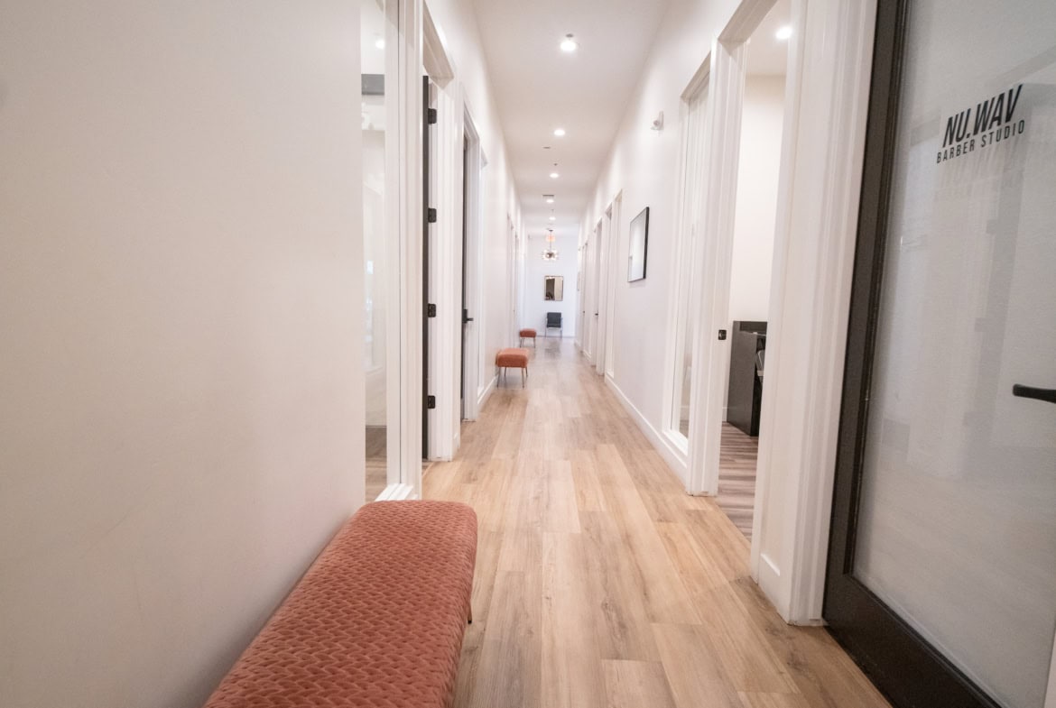Bright corridor with salon rooms and seating area, emphasizing salon rental and professional beauty services.