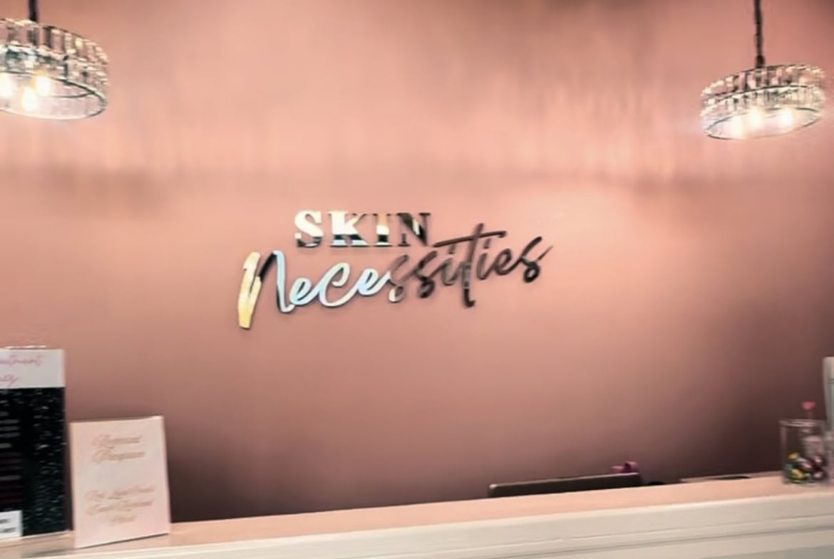 Elegant salon interior with a pink accent wall showcasing "Skin Necessities" signage. Perfect for beauty and skincare professionals.