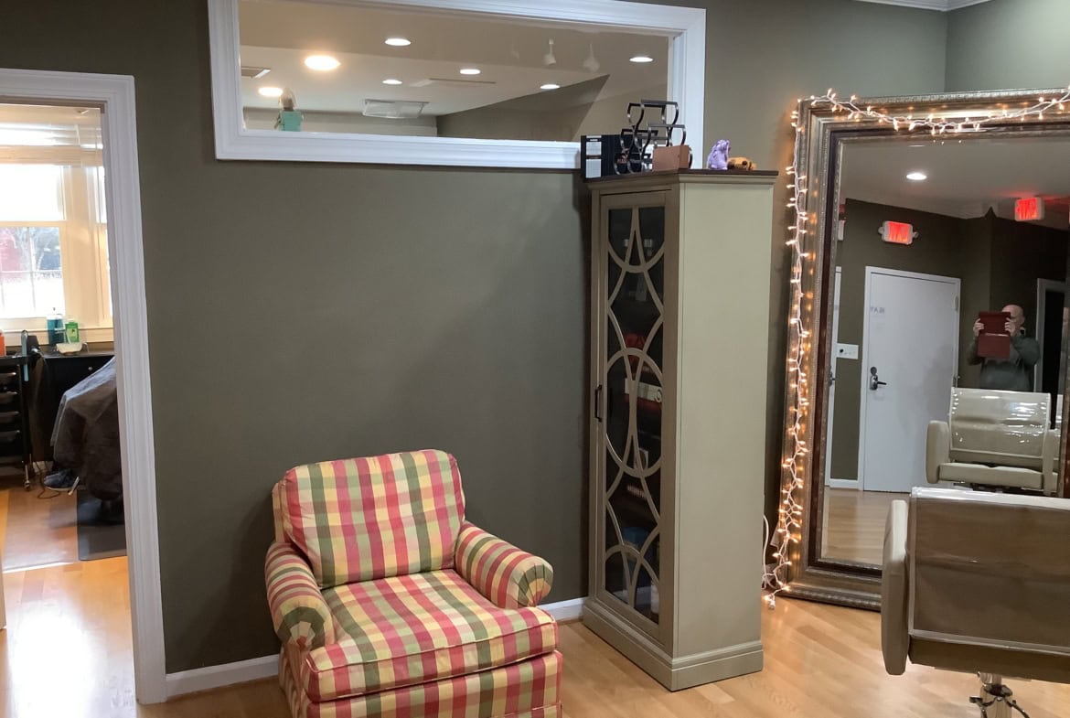 Cozy salon waiting area with a colorful plaid armchair and large mirror, perfect for a comfortable client experience.