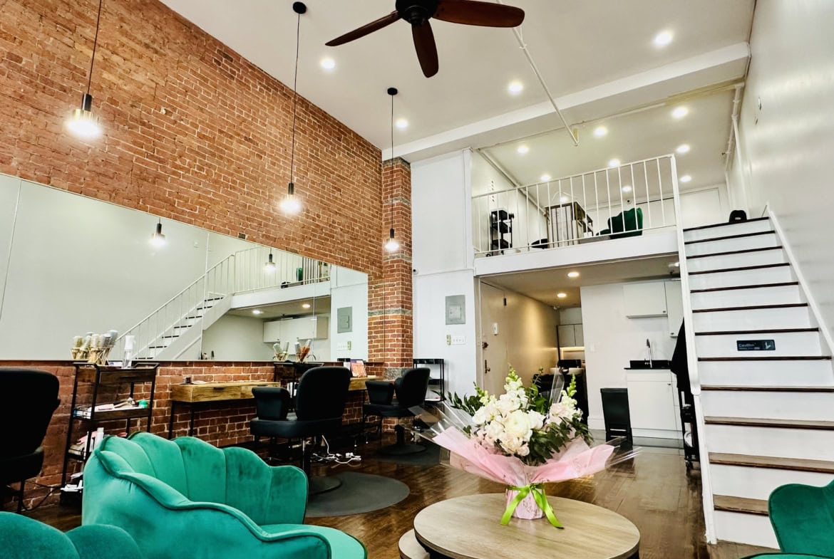 Bright modern salon interior with brick wall, seating area, and loft workspace, perfect for hair and beauty services.