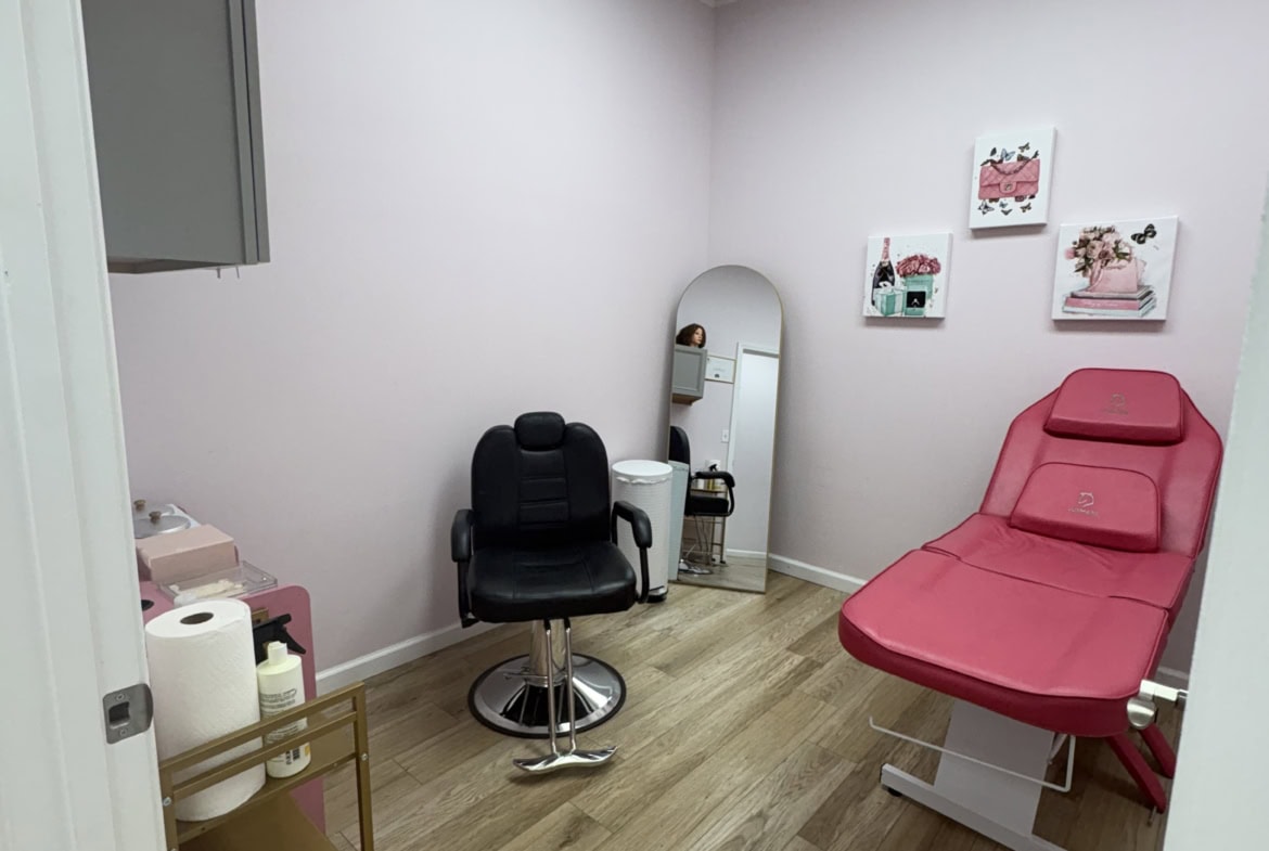 Comfortable salon treatment room with pink bed, black chair, mirror, and soft decor, ideal for beauty treatments and salon services.