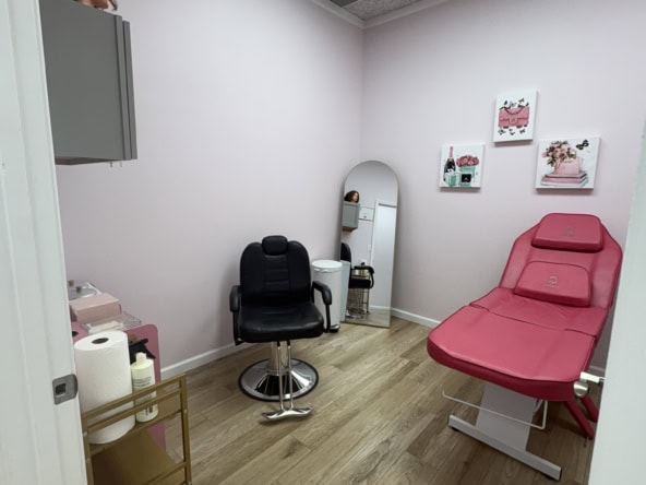 Comfortable salon treatment room with pink bed, black chair, mirror, and soft decor, ideal for beauty treatments and salon services.