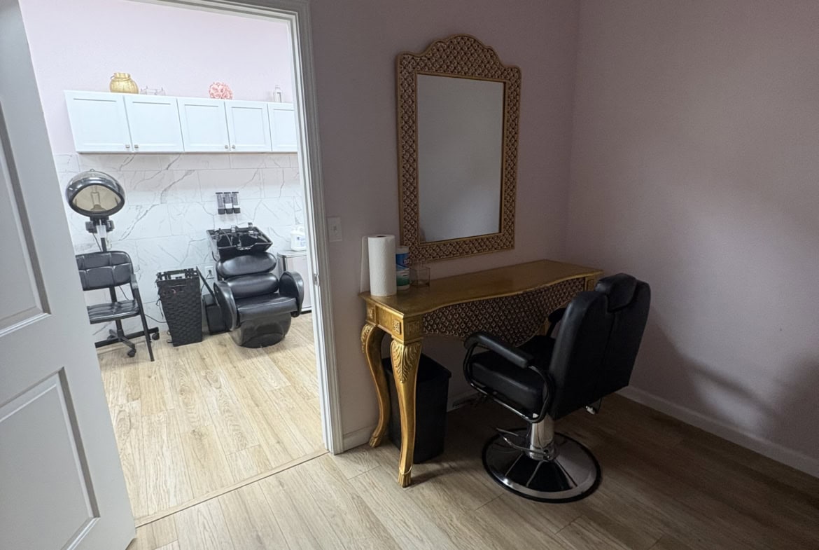 Well-lit salon rental space featuring a styling chair, mirror, and wooden desk, ideal for beauty professionals and hair stylists.