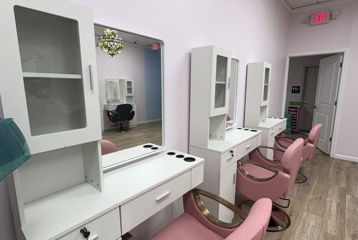 Wide view of salon styling area with modern pink chairs and white workstations for hair and beauty services.