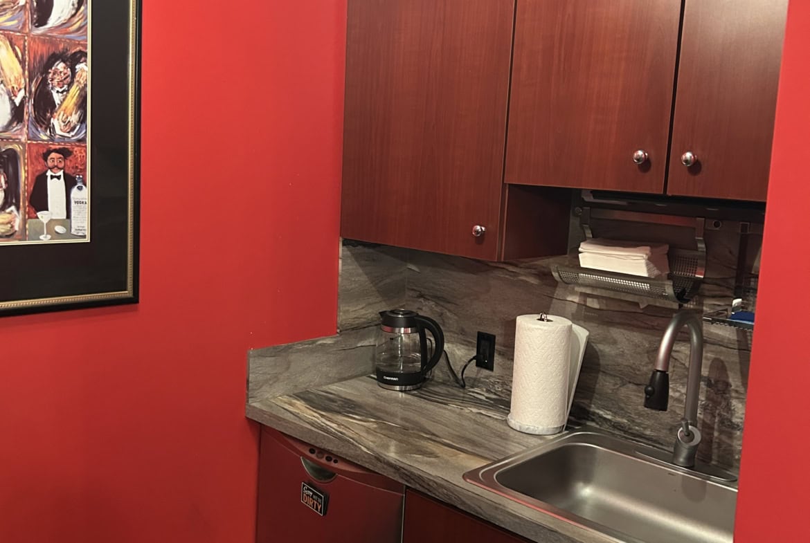 Compact salon kitchenette with red walls, wooden cabinets, sink, and coffee station.