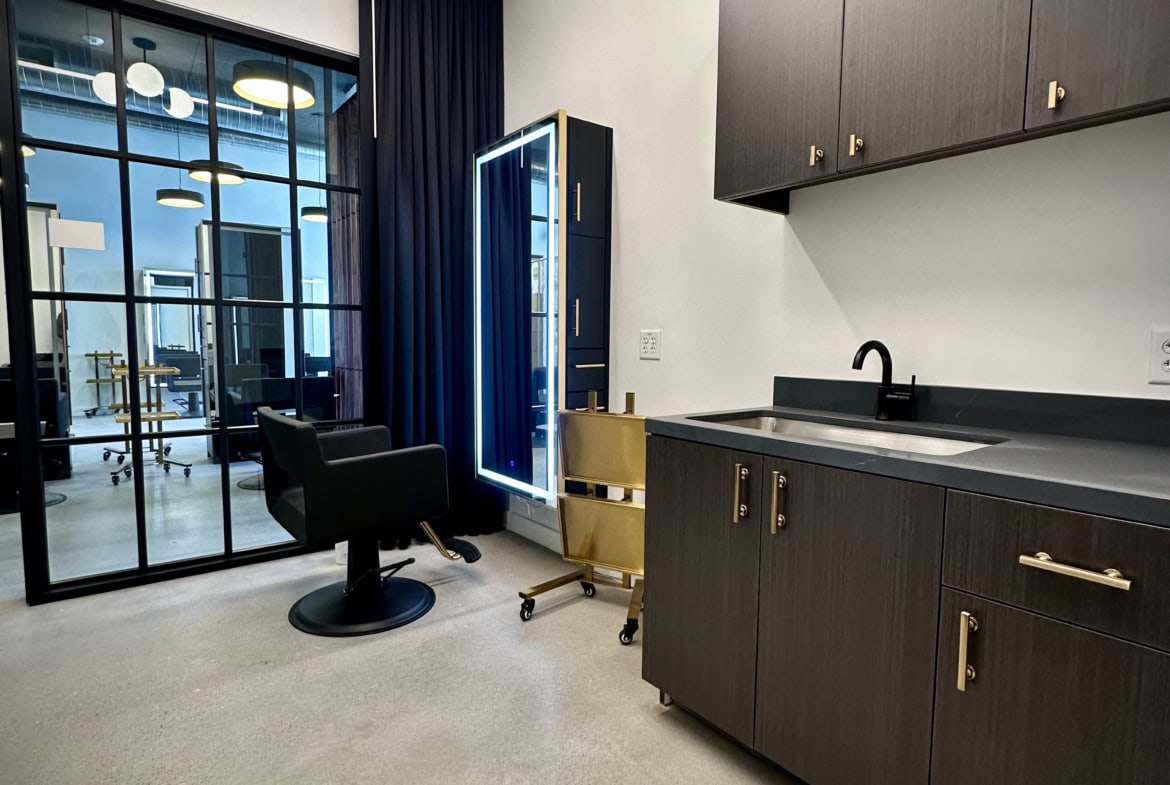 Modern salon studio with black cabinetry, sleek kitchen area, and stylish styling station.