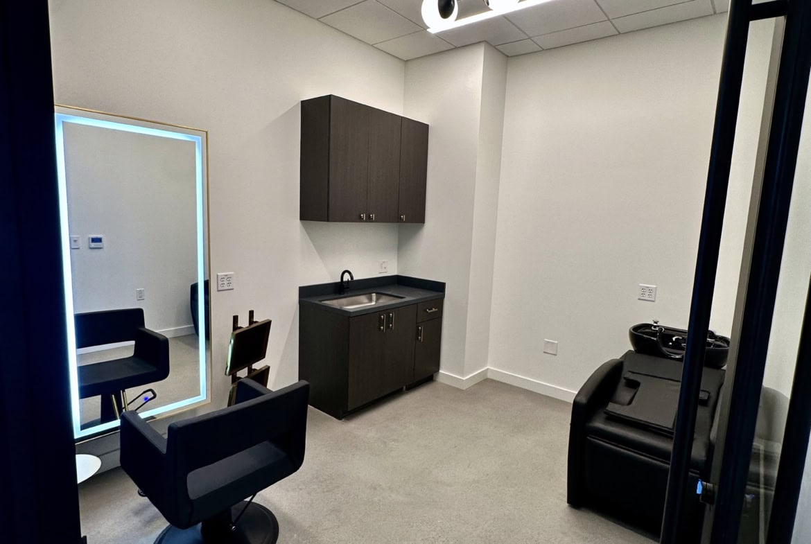 Modern salon styling station with mirror, chair, and hair washing area for rent.