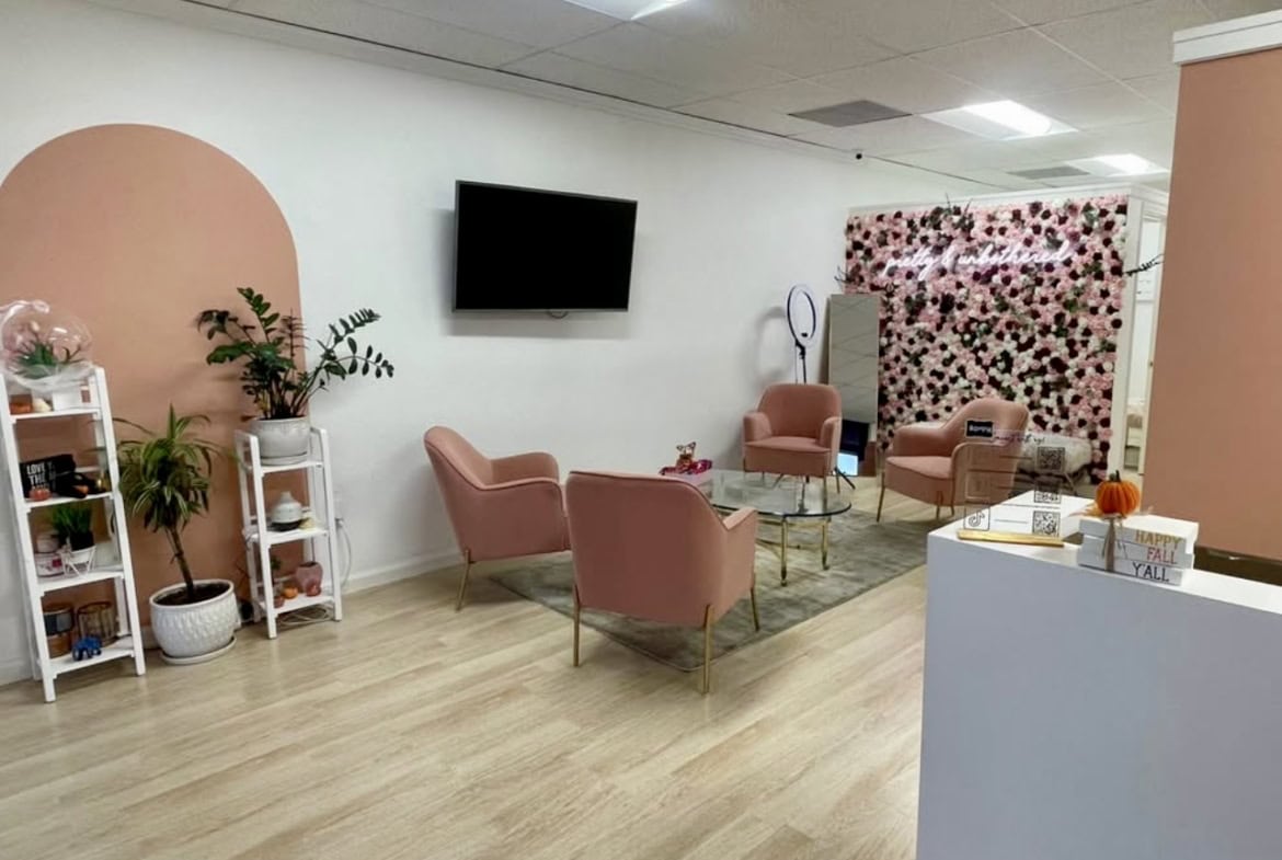 Pink salon lounge area with flower wall, cozy seating, and decorative plants, ideal for beauty or hair salon.