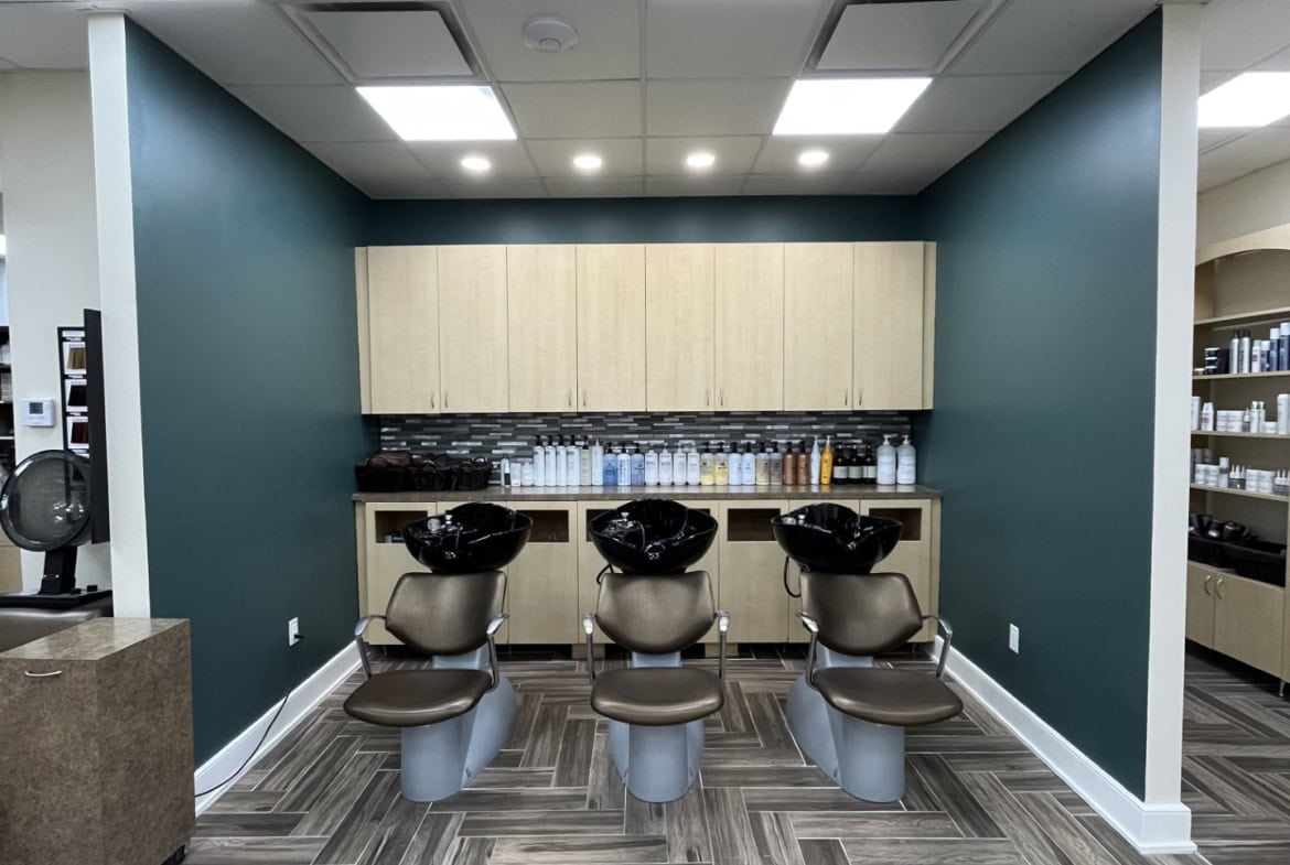 Modern salon hair washing station with three chairs and sinks, sleek cabinetry, and professional hair care products.