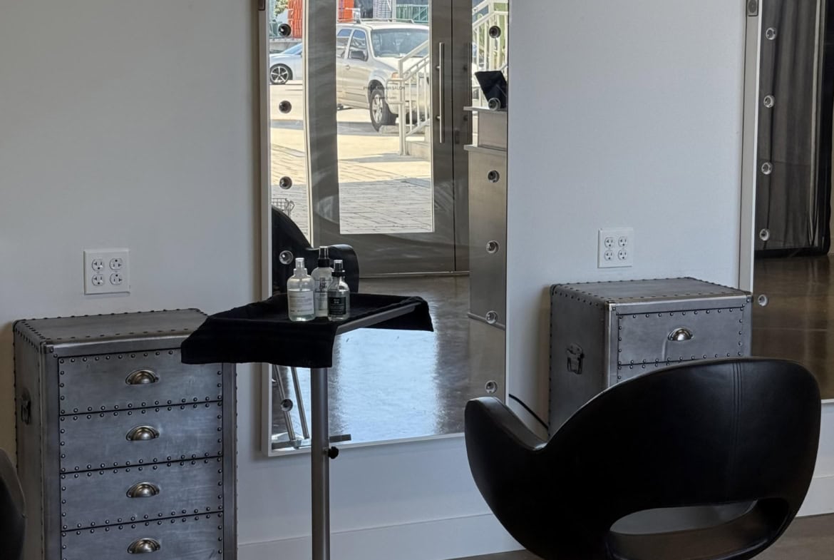Reflected salon mirror with styling station and black salon chair inside modern hair salon.
