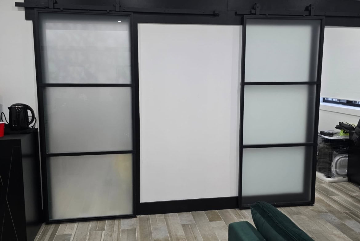 Frosted glass barn doors with black metal frame, ideal for stylish salon or studio divisions.