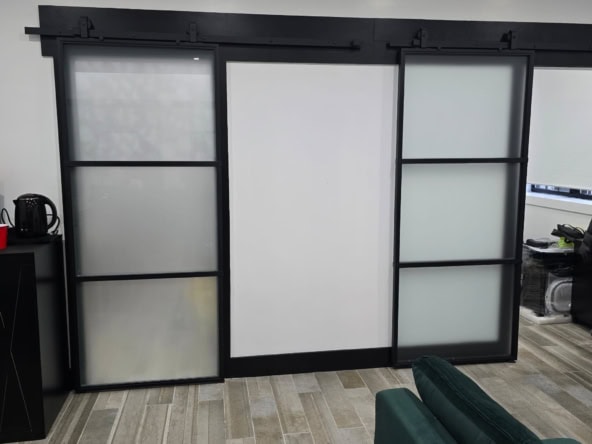 Frosted glass barn doors with black metal frame, ideal for stylish salon or studio divisions.