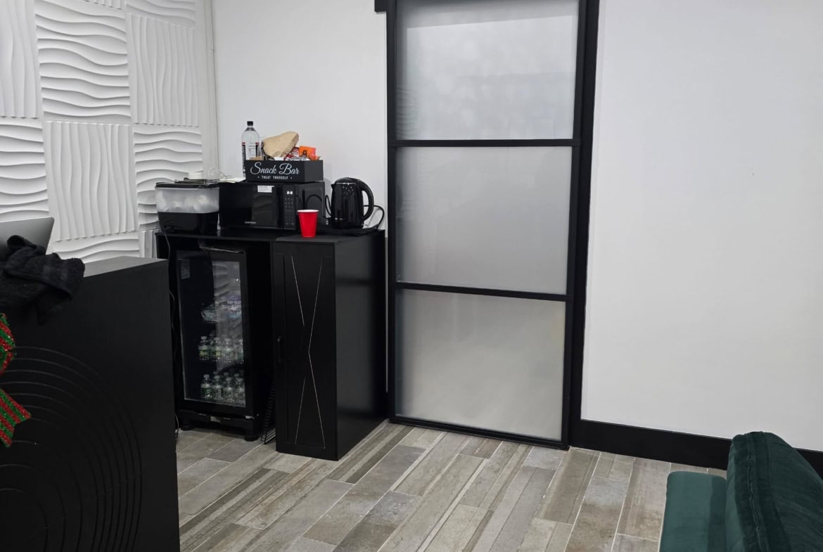 Modern salon break room with black sliding door, mini fridge, and snack bar area, ideal for salon professionals.