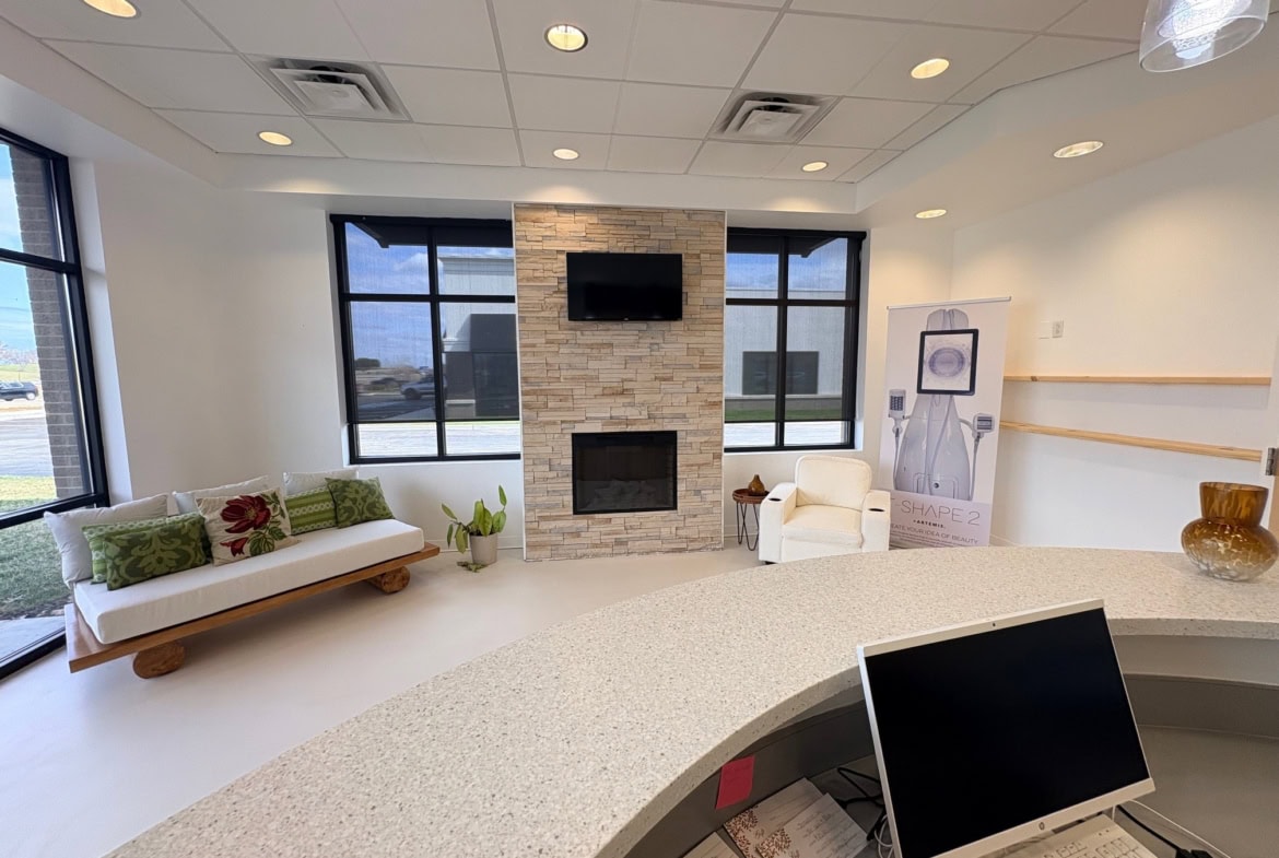 Modern salon waiting area with fireplace, large windows, and comfortable seating.