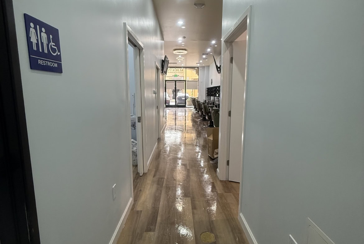 Bright salon corridor with accessible restroom sign and polished wooden floor.
