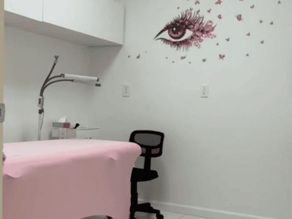 Modern salon room with a wall art of an eye and pink splashes, featuring a treatment bed, chair, and.