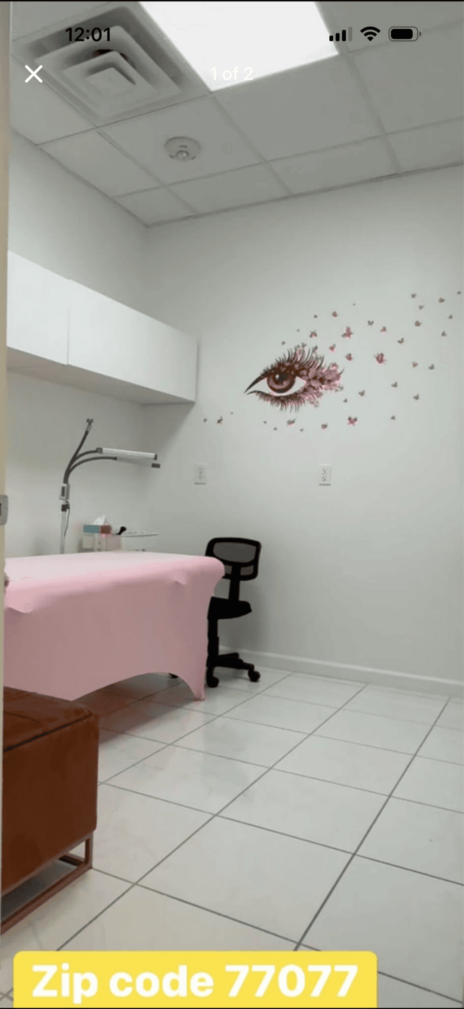 Modern salon room with a wall art of an eye and pink splashes, featuring a treatment bed, chair, and.