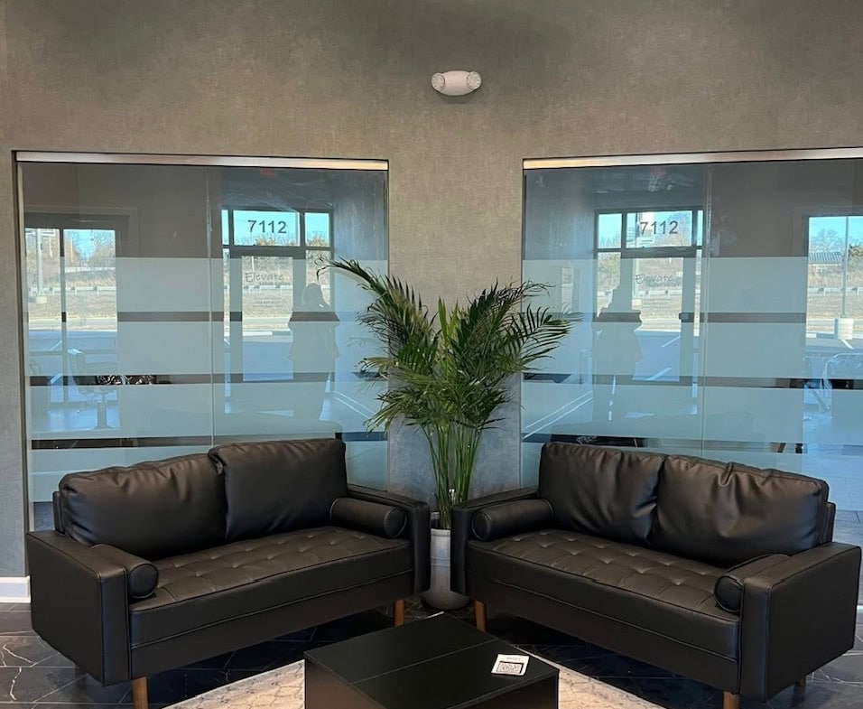 Stylish salon lounge with black leather sofas, a central coffee table, and a large potted plant.