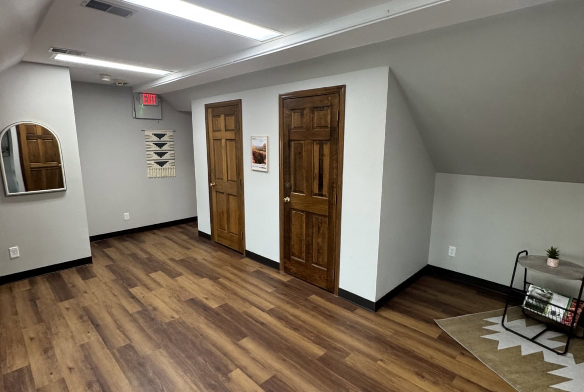 Spacious salon rental area featuring hardwood floors, white walls, and wooden doors.
