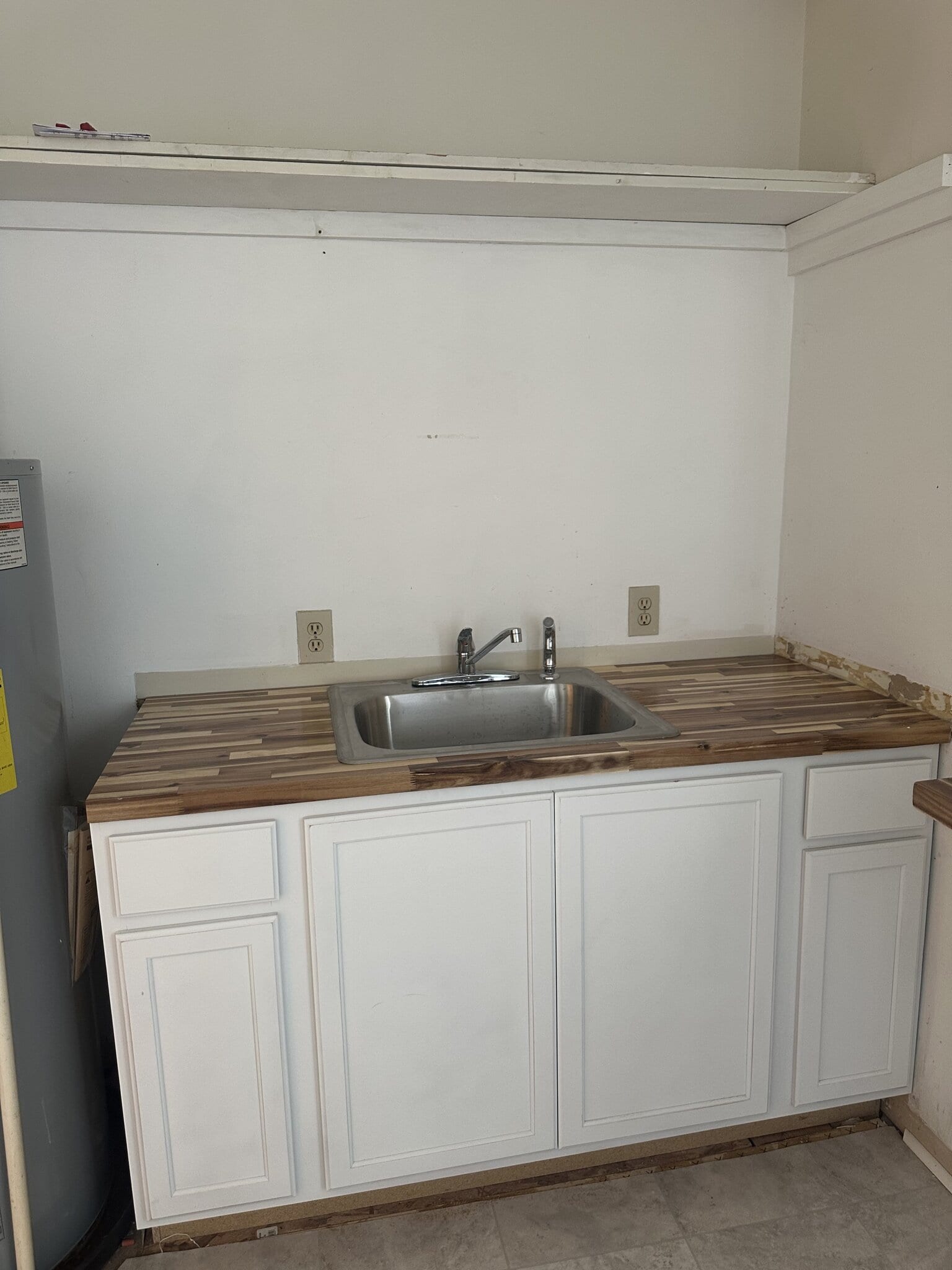 Small salon kitchenette with stainless steel sink and white cabinets.