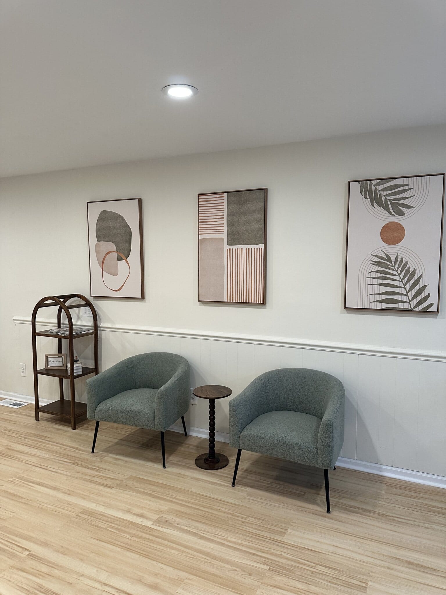 Modern salon waiting area with two teal chairs, small table, and abstract wall art.