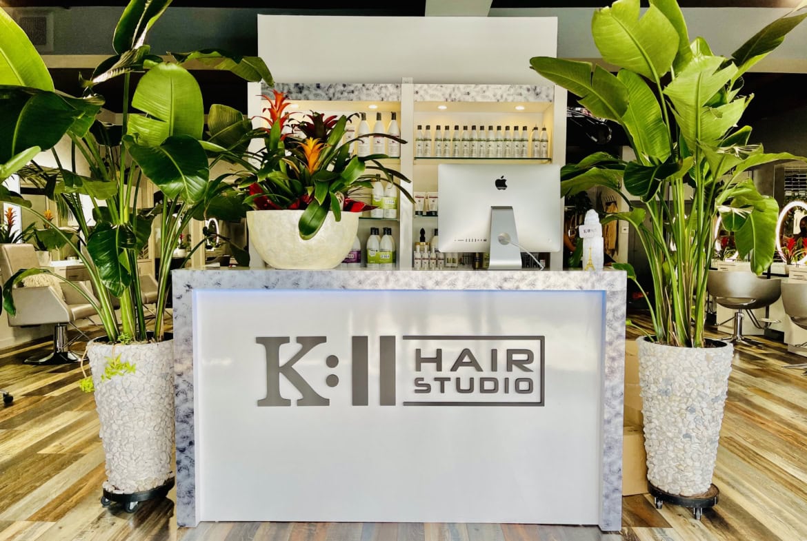 Modern salon reception area with lush green plants and a sleek white counter.
